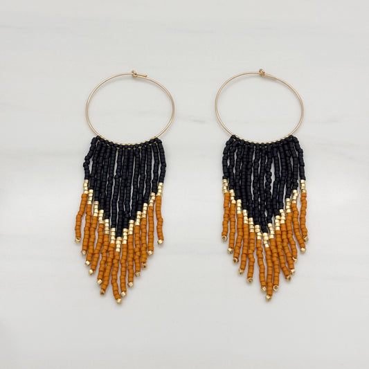 A pair of round earrings with gold-filled frames and bead fringes in black, orange, and gold colors.